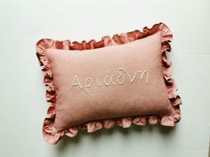 a pink pillow with embroidered name and ruffled edges sitting on a white table top