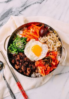 a pan filled with rice, meat and vegetables next to chopsticks on a table