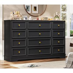 a black dresser with gold knobs in a living room next to a chair and window