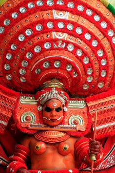 a woman dressed in red and gold with an elaborate headdress on her face