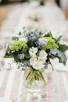 a vase filled with white and green flowers on top of a table covered in plates