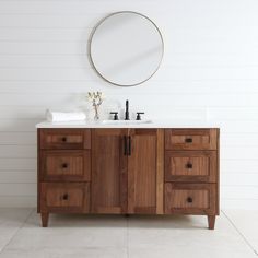 a bathroom vanity with two sinks and a round mirror on the wall above it in a white room