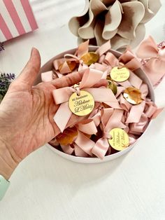 a person's hand holding a bowl of pink bows with gold tags on them