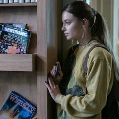 a woman standing next to a book shelf holding a cell phone