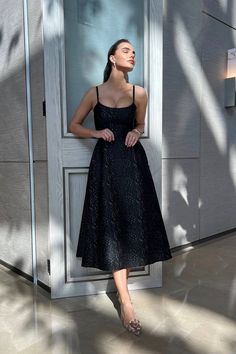 a woman standing in front of a door wearing a black dress