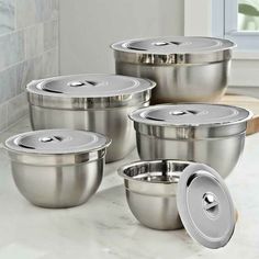 six stainless steel pots and pans with lids on a marble countertop in a kitchen