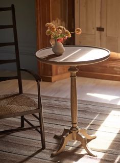 a small table with flowers on it and a chair in the back ground next to it