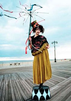 a woman standing on top of a wooden floor next to a wind spinner in front of the ocean