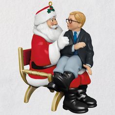 a christmas ornament with a man sitting on a chair next to a santa clause