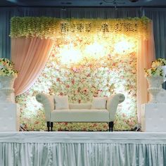 a white couch sitting in front of a stage with flowers and curtains on the wall