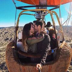 a man and woman kissing while riding in a hot air balloon over the desert with other people