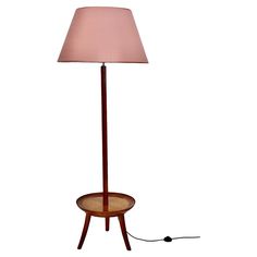 a floor lamp with a pink shade on the base and a cord plugged in