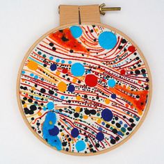 an embroidery project with colorful circles and lines on the hoop hanging from a wooden hanger