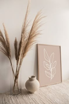 a vase with some dry grass in it next to a framed photograph on the wall