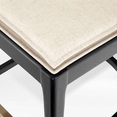 an upholstered stool with a beige cushion on the top and black metal legs