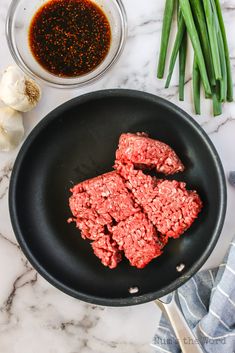 raw ground beef in a skillet next to green onions and garlic on a marble countertop