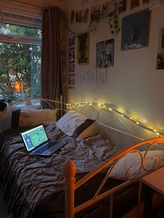 a laptop computer sitting on top of a bed in a room with pictures and string lights