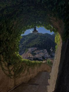 an archway with vines on it leading to a town below the trees and mountains in the distance