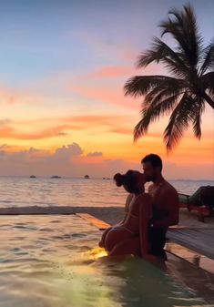 a man and woman sitting on the edge of a pool in front of an ocean