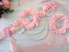 pink flowers and pearls are arranged on a white table with ribbon, beads and ribbons