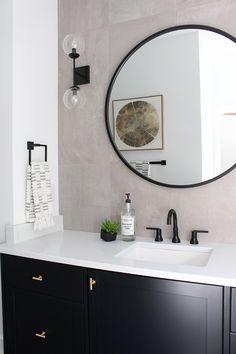 a bathroom with a large round mirror above the sink and black cabinetry, along with a white counter top