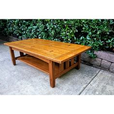 a wooden table sitting on top of a sidewalk next to a green bush and shrubbery