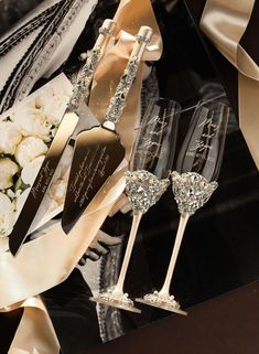 two champagne flutes sitting next to each other on top of a black table with white flowers