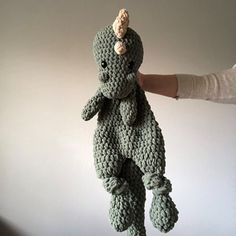 a crocheted stuffed animal is being held by a person's hand in front of a white wall