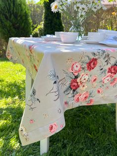 a table covered with a flowered cloth in the grass next to a potted plant