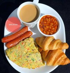 a white plate topped with breakfast foods next to cups of coffee and croissants