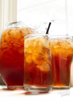 two glasses filled with iced tea sit next to each other on a window sill