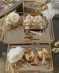 two gold trays with white flowers and feathers on them are sitting on a table