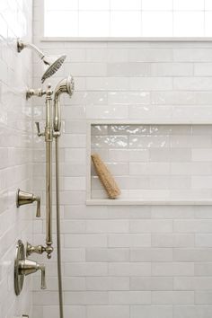 a white tiled bathroom with a window and shower head