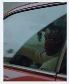 a man sitting in the passenger seat of a red car with his head out the window