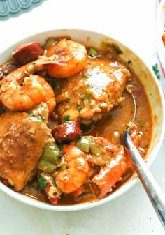 a bowl filled with shrimp and vegetables on top of a white tablecloth next to a spoon