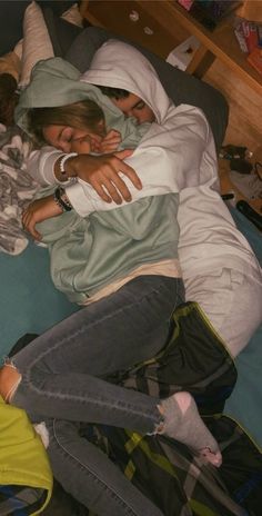 two people are laying on a bed with their arms wrapped around each other and hugging