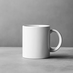 a white coffee mug sitting on top of a table next to a gray and white wall