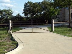 a gated walkway leads to an old brick building with trees in the back ground