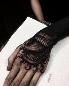 a person's hand with a black and white tattoo design on it, which has an open mouth