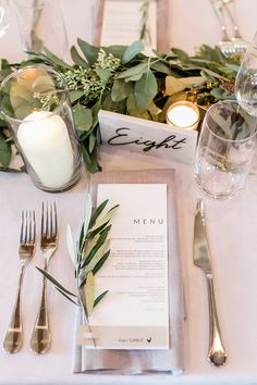 the table is set with silverware, candles and greenery for an elegant dinner