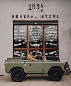 a man sitting in the driver's seat of a green jeep parked next to a building