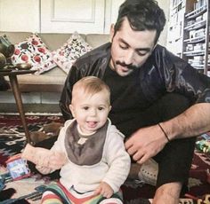 a man sitting next to a baby on top of a rug