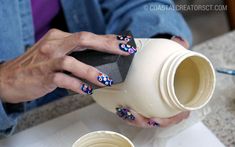 a woman is holding a cup with flowers painted on it and her nails are done