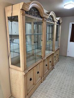 a wooden china cabinet with glass doors and drawers on the front, in an empty room