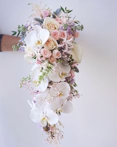 a bouquet of flowers hanging from the side of a white wall in front of a person's hand