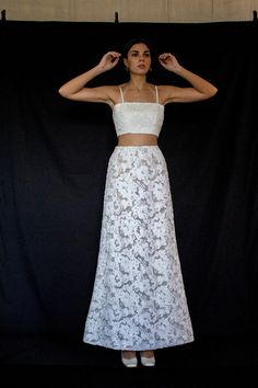 a woman standing in front of a black backdrop wearing a white skirt and crop top