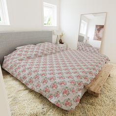 a bed with pink flowers on it and a mirror in the corner behind it that is next to a window