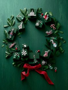 a wreath made out of green boxes with red ribbon and ornaments hanging from the sides