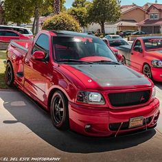 a red pick up truck parked in a parking lot next to other cars and trees