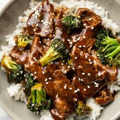 beef and broccoli with sesame seeds on top of white rice in a bowl